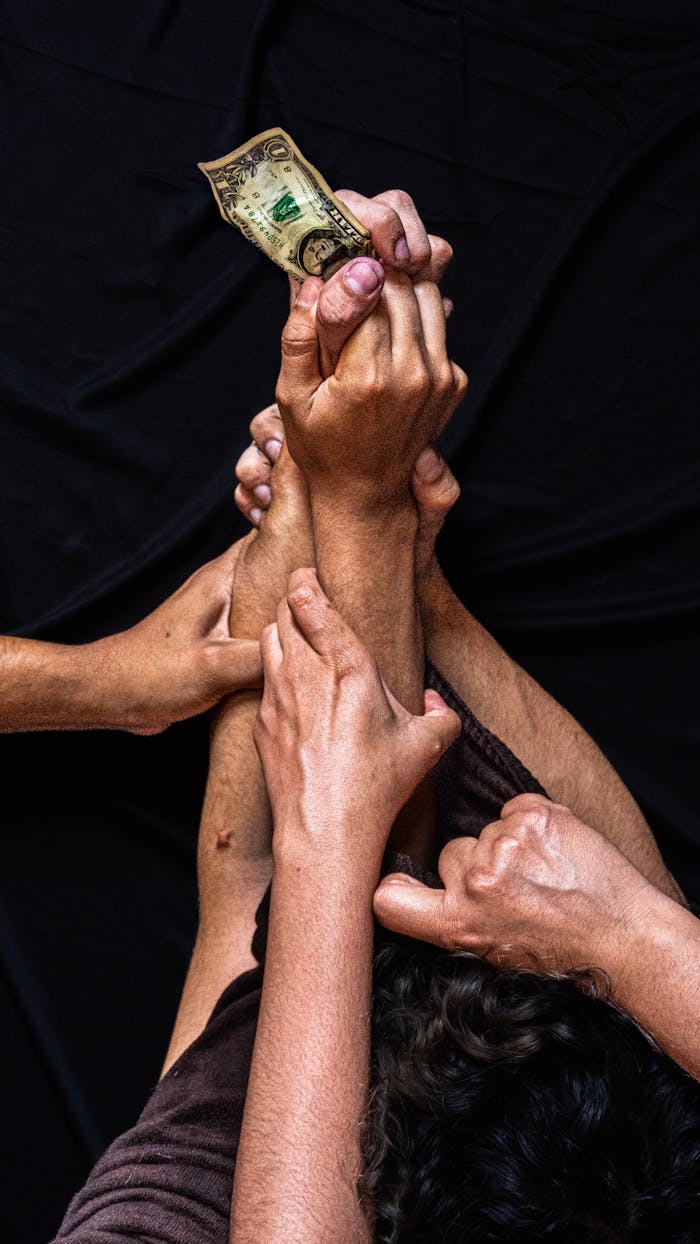 Close-up of multiple hands reaching for a single dollar bill, symbolizing financial competition or struggle.